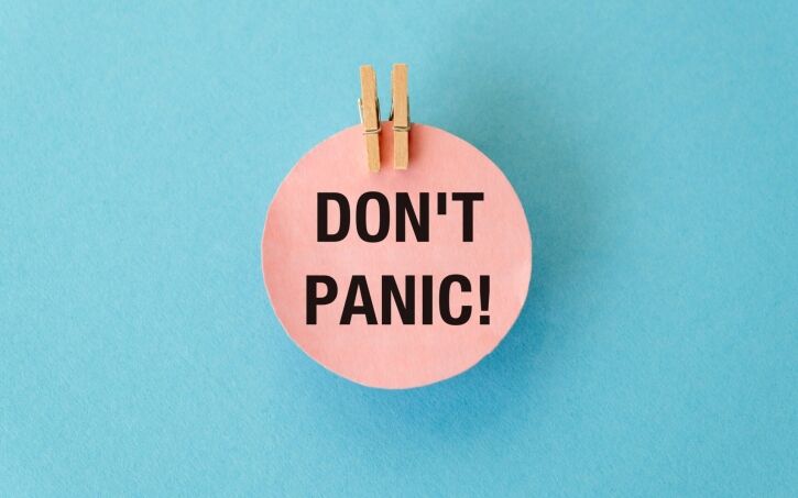 A piece of pink paper with the words Don't Panic written on it and held with pegs
